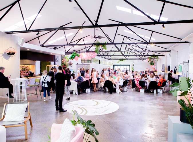 People gathered in a spacious room, sitting around tables and chairs at a Christening venue in Melbourne.