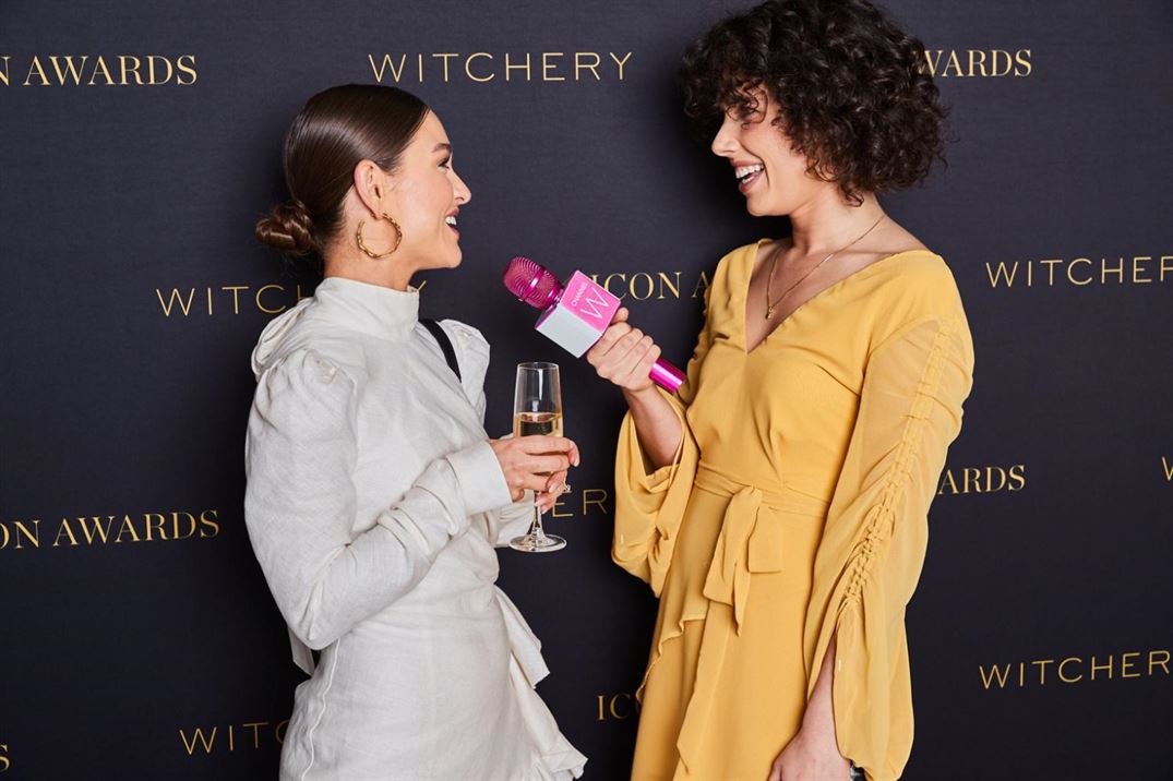 Two women chatting on a red carpet at a fashion runway venue.