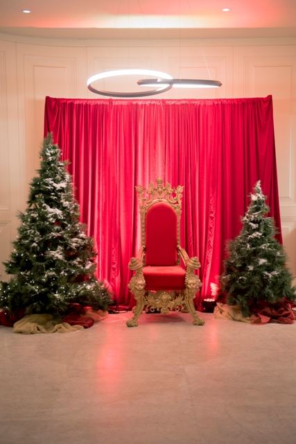 A festive red chair with a matching curtain, surrounded by two trees. Perfect for function spaces in Melbourne Christmas parties!
