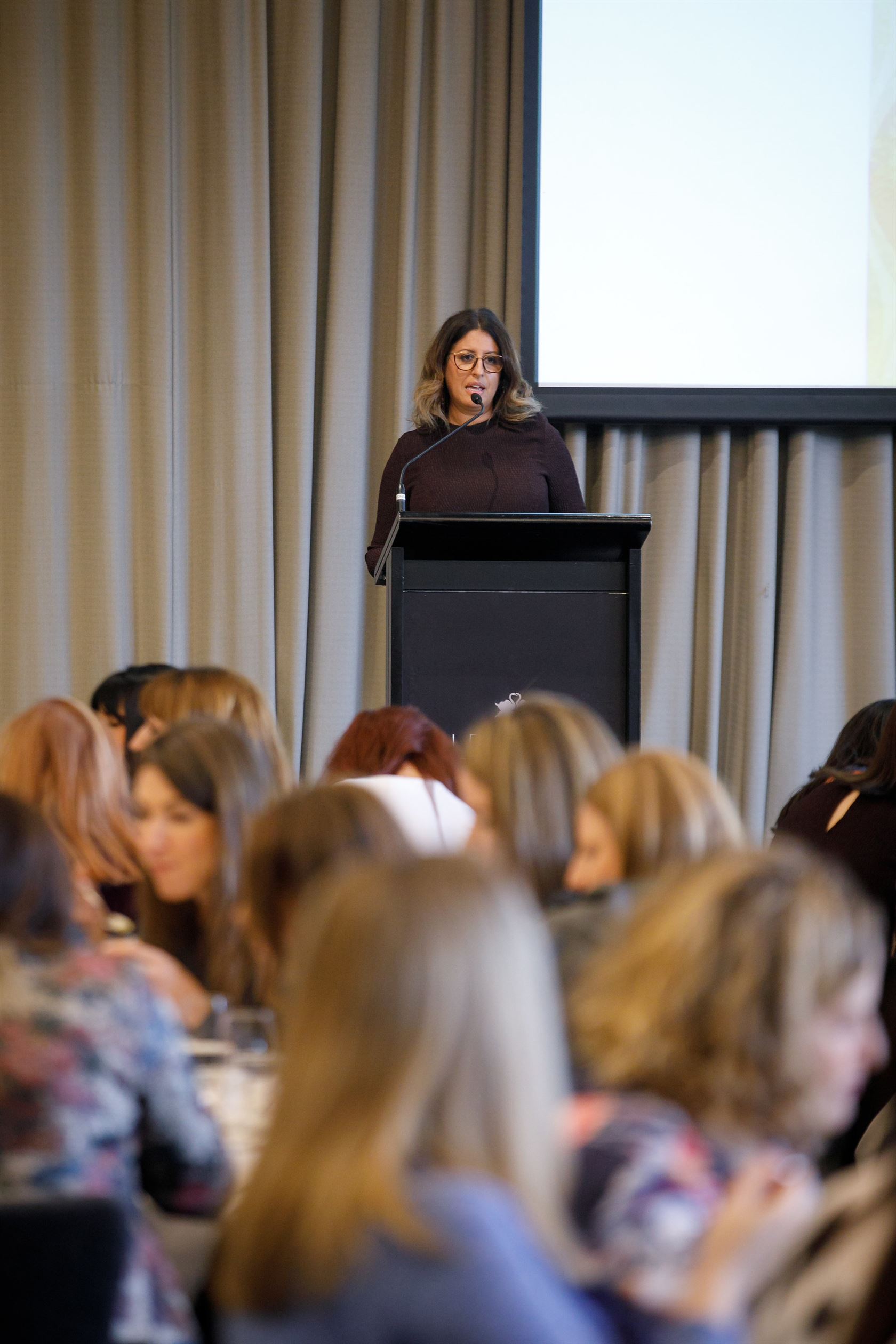 A woman confidently presenting at a conference in Melbourne. She captivates the audience with her engaging presentation skills.