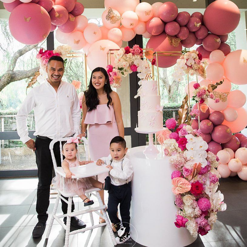A happy family captures a moment in front of a beautiful pink and white balloon arch at one of the Christening venues in Melbourne.