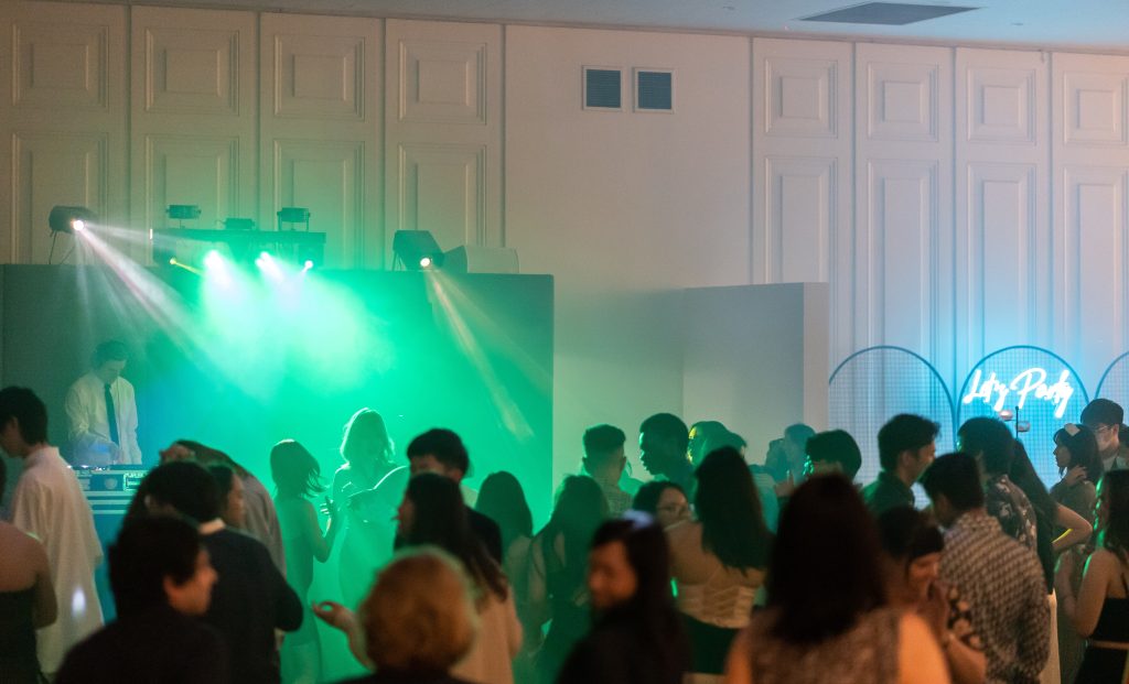 A lively school event with a big crowd of people enjoying a party atmosphere, illuminated by vibrant green lighting.