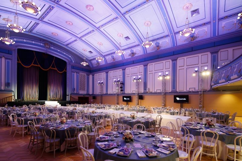 A bustling banquet hall filled with set tables, enjoying an event in a large room.
