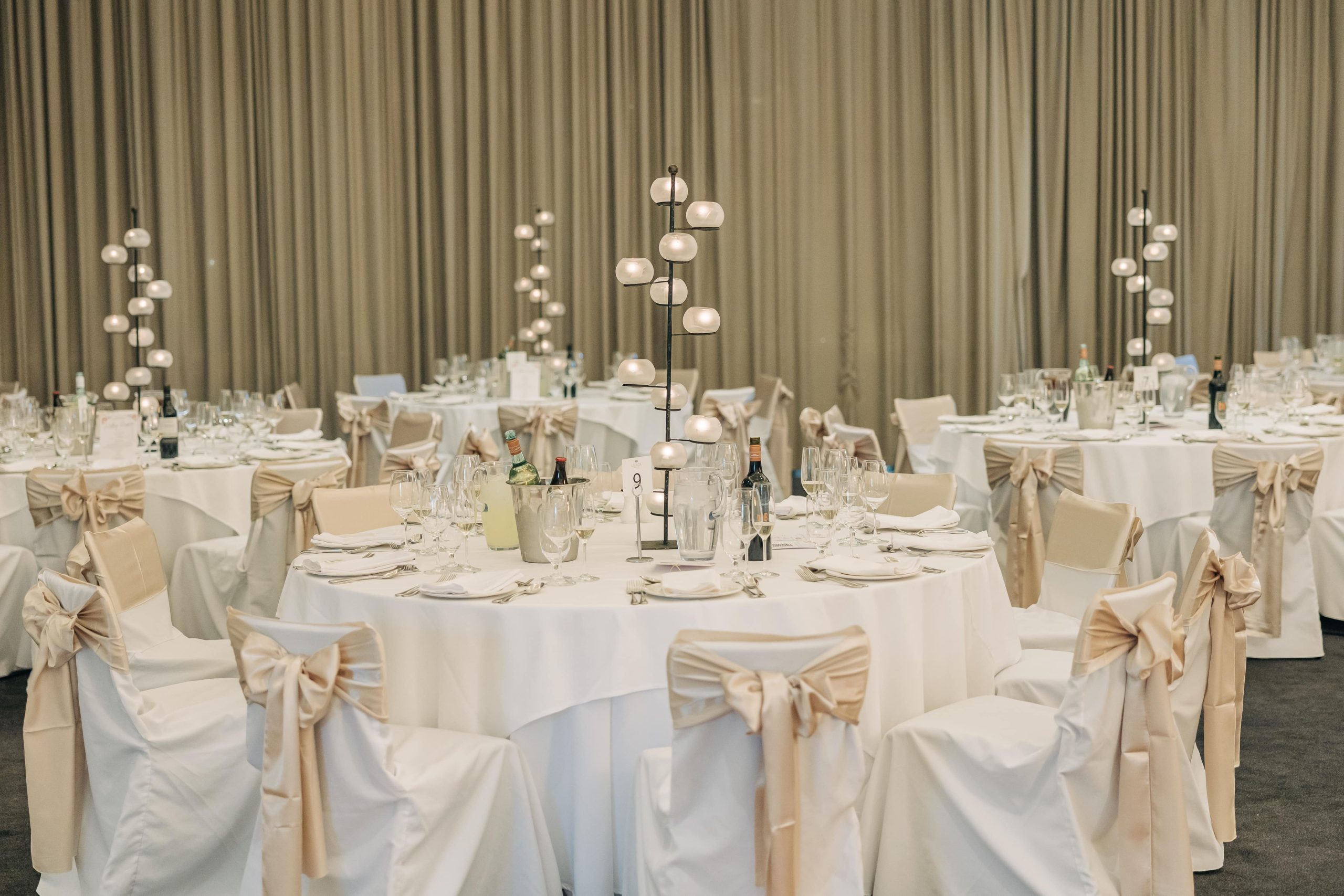 A timeless ballroom set with fresh white linen and chairs with gold sashes, perfect for an event in Melbourne